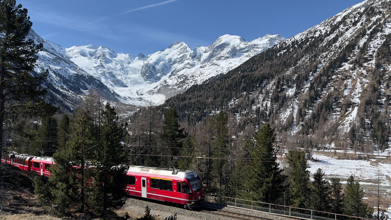 Red Bernina Express train traversing snowy Swiss Alps against a scenic backdrop.