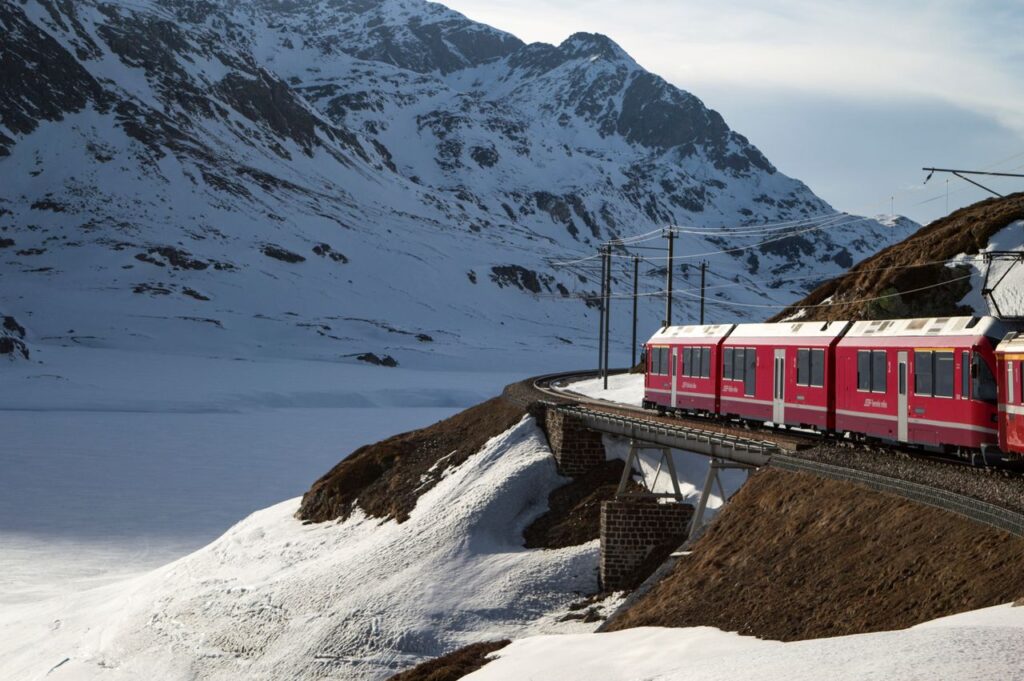 Red Bernina Express train traversing snowy mountains in the Swiss Alps during winter.