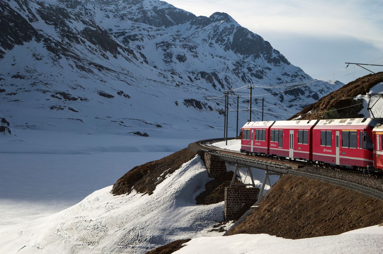 Red Bernina Express train traversing snowy mountains in the Swiss Alps during winter.