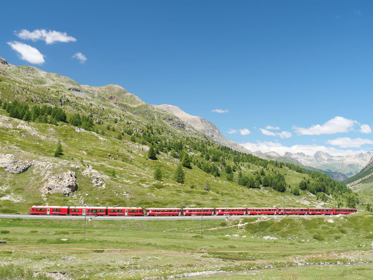Experience the breathtaking view of a red train traversing the picturesque Bernina Pass in Switzerland's Alps.