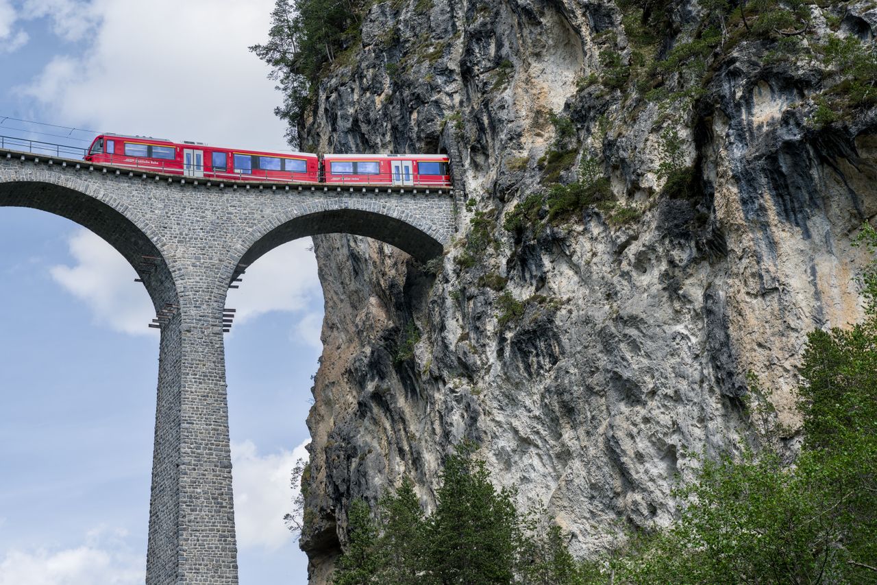 Red train crossing iconic Landwasser Viaduct in Swiss Alps, a breathtaking engineering marvel.