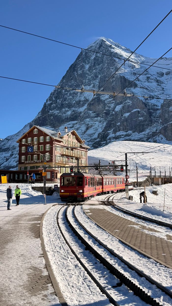 Red train at Grindelwald station with snowy mountains in the background. Winter travel in Switzerland.